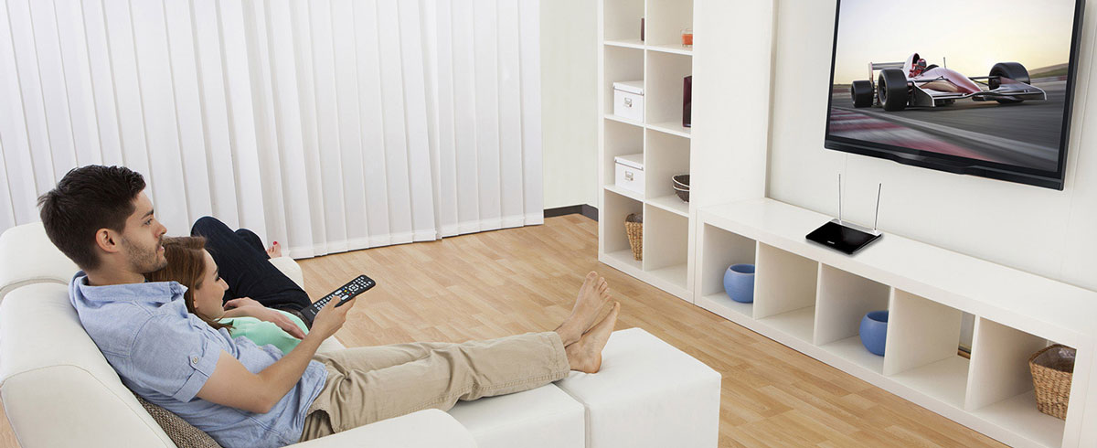 A man and woman are seated on a couch, watching the television