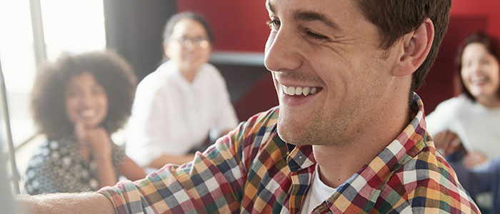 Close-up of a smiling man&rsquo;s face, with four people out-of-focus in the background.